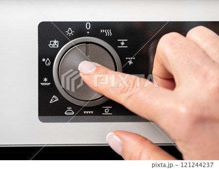 Woman adjusting modern white oven in kitchen. Female hand pushing and turning knobs on oven control panel Woman adjusting modern white oven in kitchen. Female hand pushing and turning knobs on oven control panel 121244237