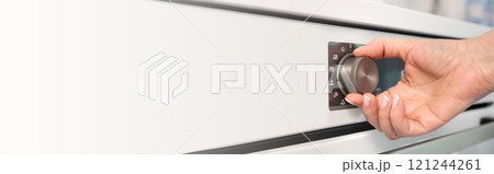 Woman adjusting modern white oven in kitchen.  Female hand pushing and turning knobs on oven control panel. Long banner 121244261