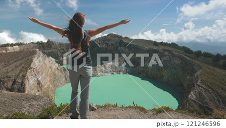 Female tourist is embracing the beauty of nature while standing on the edge of a crater lake with turquoise water. She is enjoying the view of the volcano crater in the philippines Female tourist is embracing the beauty of nature while standing on the edge of a crater lake with turquoise water. She is enjoying the view of the volcano crater in the philippines 121246596