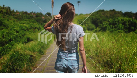 Young woman is enjoying a sunny day walking on the campuhan ridge walk in ubud, bali, indonesia. She is surrounded by lush green vegetation and the sun is shining brightly Young woman is enjoying a sunny day walking on the campuhan ridge walk in ubud, bali, indonesia. She is surrounded by lush green vegetation and the sun is shining brightly 121246603