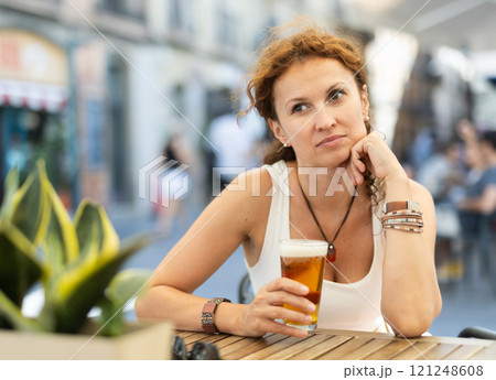 Relaxed woman sitting with beer at table in outdoor cafe 121248608