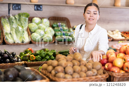 Delighted young woman purchaser choosing kiwi in grocery store 121248820