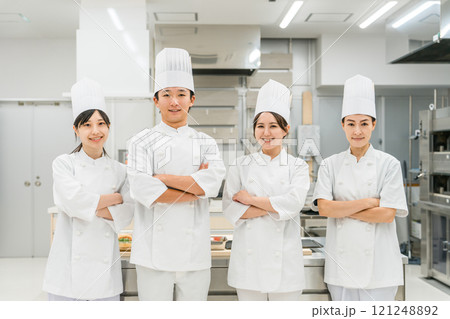 厨房・キッチンに立つコックコート姿の調理師・シェフ・コックの男女（腕組み） 121248892