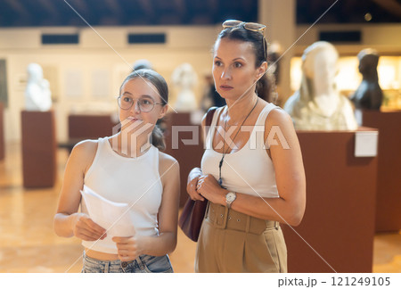 Young woman with teen daughter walk around museum, view sculpture in museum hall 121249105