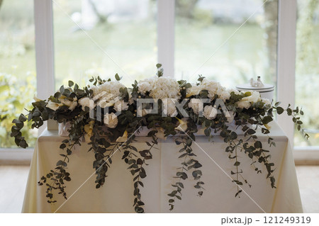 A table with a white tablecloth and a floral arrangement of white flowers 121249319