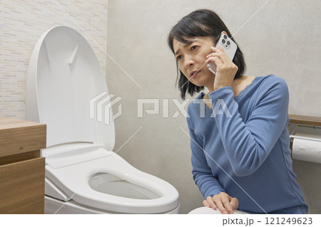 トイレで修理業者に電話をする女性 トイレで修理業者に電話をする女性 121249623