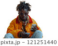 A man in a yellow jacket sits on the ground and looks at his phone 121251440
