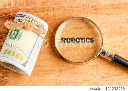 The concept of technology and development. Phrase, words, text ROBOTICS through a magnifying glass on an antique background, top view 121252056
