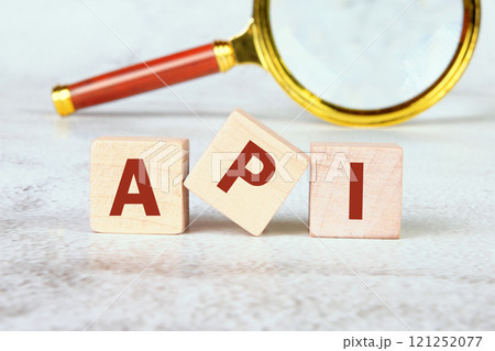 API abbreviation, modern technology concept. API written on wooden cubes with a magnifying glass in the background API abbreviation, modern technology concept. API written on wooden cubes with a magnifying glass in the background 121252077