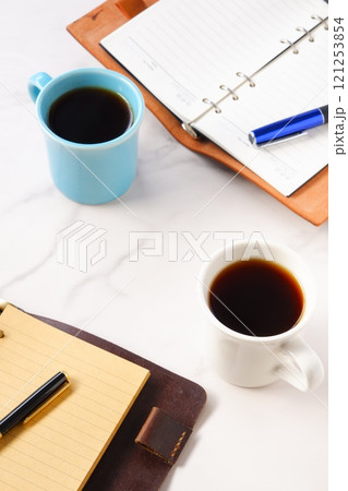 コーヒーが入ったふたつのマグカップとシステム手帳で、ふたりがコーヒーを飲みつつ打ち合わせ中のイメージ コーヒーが入ったふたつのマグカップとシステム手帳で、ふたりがコーヒーを飲みつつ打ち合わせ中のイメージ 121253854