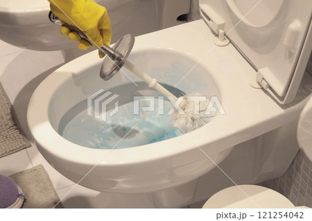 Woman in yellow rubber gloves scrub toilet bowl with brush and cleaner. House cleaning. Interior of house. Woman in yellow rubber gloves scrub toilet bowl with brush and cleaner. House cleaning. Interior of house. 121254042