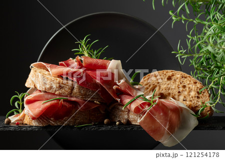 Ciabatta with prosciutto and rosemary on a black background. 121254178