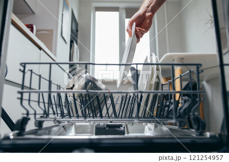 Male hand putting dirty plate in dishwasher, view from inside dishwasher. Household chores, man washing dishes Male hand putting dirty plate in dishwasher, view from inside dishwasher. Household chores, man washing dishes 121254957