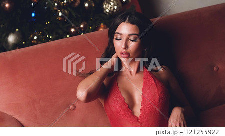 Beautiful brunette posing sexy on camera in red lace bodysuit while sitting on sofa Beautiful brunette posing sexy on camera in red lace bodysuit while sitting on sofa 121255922