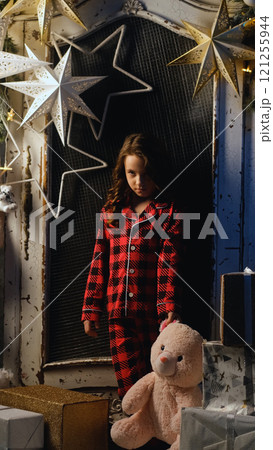 Portrait of sad dissatisfied little girl in night pajamas holding teddy bear in hands. Child disappointed with gifts from Santa Claus. Christmas night, festive atmosphere 121255944
