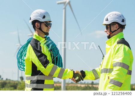 Team of professional electrical engineers in fully safety suit are working and discussing together at the windmill electric generating turbine. Electricians working at the site of windmill turbine. Team of professional electrical engineers in fully safety suit are working and discussing together at the windmill electric generating turbine. Electricians working at the site of windmill turbine. 121256400