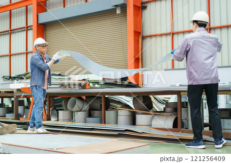 Asian specialist technicians or engineers are working in the metal sheet blending factory. Engineers perform inspection at raw metal sheet after rolling out from the blending machine. 121256409