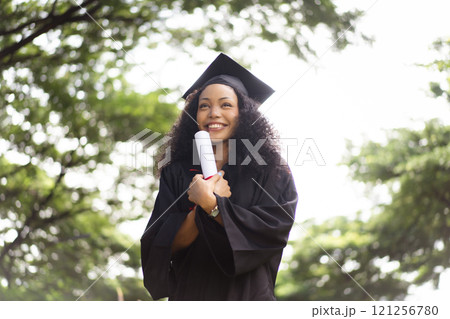 Female student in graduation gown has an excited and delighted expression as she receives her diploma upon graduating from university. African woman feels proud about her academic achievement. Female student in graduation gown has an excited and delighted expression as she receives her diploma upon graduating from university. African woman feels proud about her academic achievement. 121256780