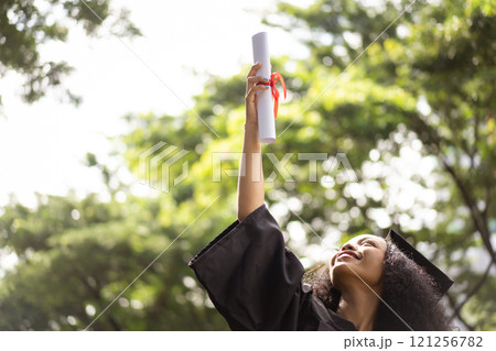 Female student in graduation gown has an excited and delighted expression as she receives her diploma upon graduating from university. African woman feels proud about her academic achievement. Female student in graduation gown has an excited and delighted expression as she receives her diploma upon graduating from university. African woman feels proud about her academic achievement. 121256782