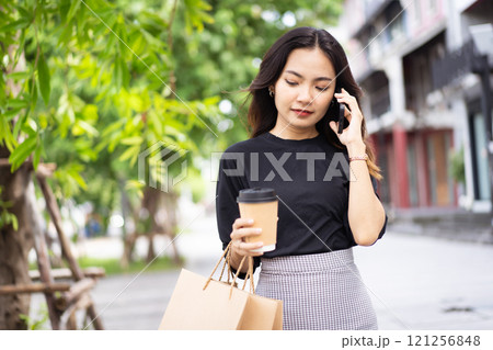 Smart and good looking Asian businesswoman is walking in the city while using a smartphone for text message and talking to colleague and other hand holding a coffee cup. Business woman portrait. 121256848