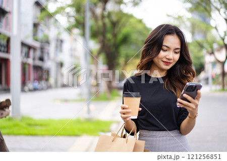 Smart and good looking Asian businesswoman is walking in the city while using a smartphone for text message and talking to colleague and other hand holding a coffee cup. Business woman portrait. Smart and good looking Asian businesswoman is walking in the city while using a smartphone for text message and talking to colleague and other hand holding a coffee cup. Business woman portrait. 121256851