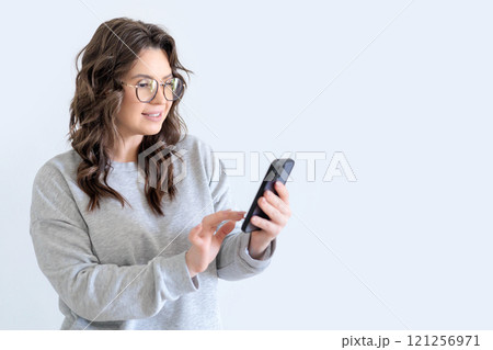 Beautiful European woman in gray knitted suit smiles and writes a message in messenger on smartphone Beautiful European woman in gray knitted suit smiles and writes a message in messenger on smartphone 121256971