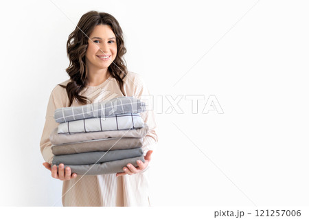 Young European beautiful woman holds neat stack of stylish bed linen in natural colors. 121257006