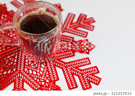 A transparent mug of coffee, in which foam and a bottle are visible, stands on a red napkin in the form of a snowflake on a white background in close-up with space for text. High quality photo 121257013