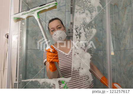 A woman is diligently cleaning the shower glass in a modern and stylish bathroom space 121257617