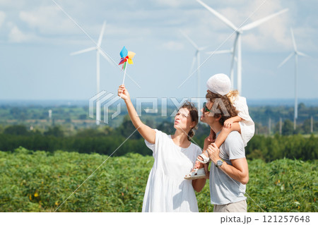 Caucasian family in vacation activity. Happy cheerful caucasian white family with daughter are walking and relaxing together in the daytime in nature with windmill towers in background.  121257648