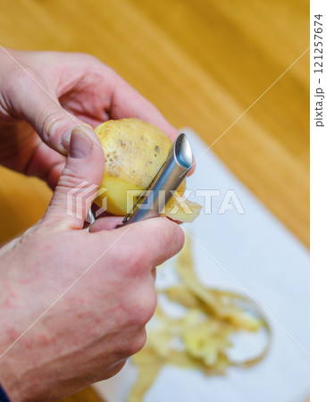 Close-up of a person peeling a potato with a vegetable peeler. High quality photo 121257674
