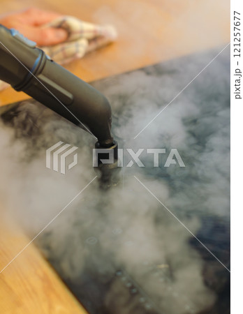 Close-up of a steam cleaner nozzle releasing steam onto induction stove . High quality photo 121257677