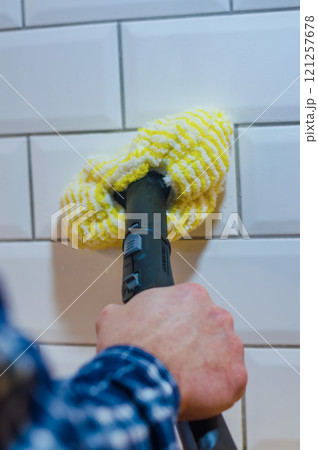Man cleaning white tile wall with a yellow microfiber cloth and steam cleaner. High quality photo 121257678