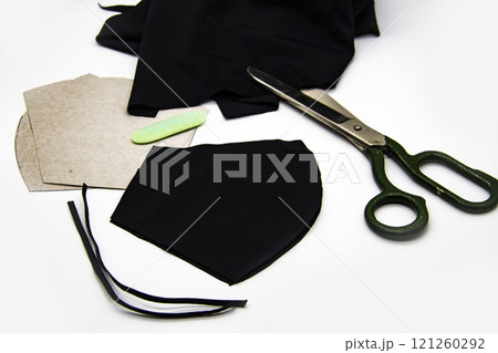 Preparation for sewing a black mask in quarantine at home against white background. Black fabric, blanks for masks, scissors and the soap 121260292