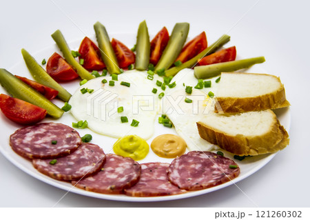 Delicious breakfast with eggs, salami, cucumbers, cherry tomatoes, slices of loaf, sauces and green onion on top on a white plate. Healthy and tasty meal for breakfast or lunch. 121260302