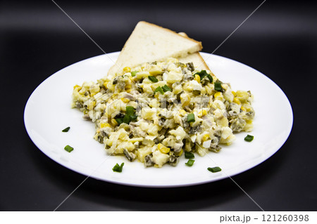 Ukrainian and Russian salad Olivier according to a new recipe on a white plate. Healthy salad Olivier with meat, corn and slices of white bread. Delicious and tasty salad on white plate. 121260398