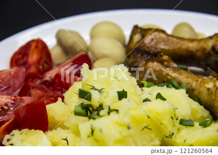 Tasty cooked chicken legs with potatoes, tomatoes, mushrooms on a white plate. Delicious potatoes with onion and dill on dinner, lunch. Amazing chicken legs cooked in spice. Ukrainian healthy meal 121260564