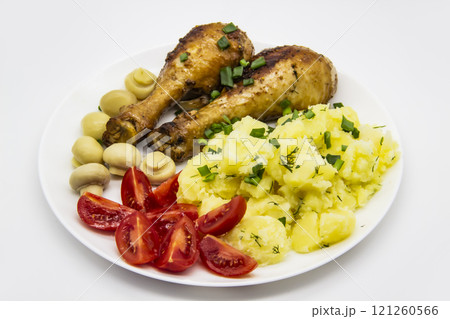 Tasty cooked chicken legs with potatoes, tomatoes, mushrooms on a white plate. Delicious potatoes with onion and dill on dinner, lunch. Amazing chicken legs cooked in spice. Ukrainian healthy meal 121260566