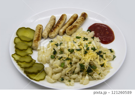 Pasta on a plate with cheese on top and green onions. Delicious pasta made from high quality flour with chicken sausage from grill and sliced cucumber from jar. Horns made of flour cooked with cheese, 121260589