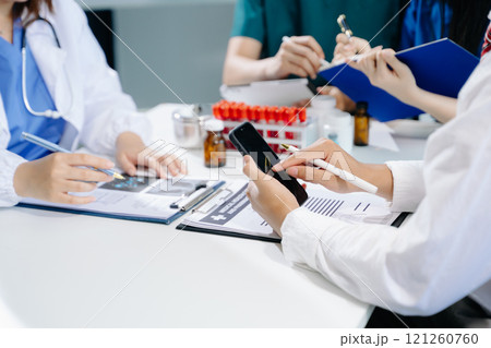 Medical team having a meeting with doctors in white lab coats and surgical scrubs seated 121260760