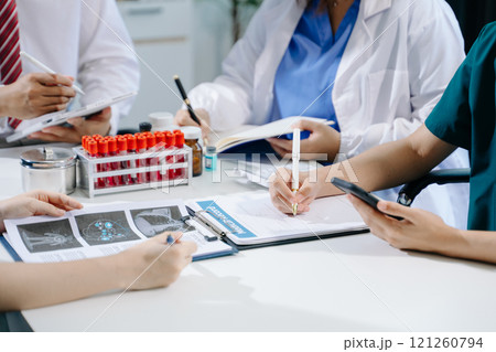 Medical team having a meeting with doctors in white lab coats and surgical scrubs seated 121260794