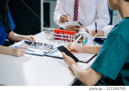 Medical team having a meeting with doctors in white lab coats and surgical scrubs seated 121260795