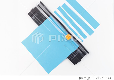 Paper trimmer cutting blue cardstock into strips on a white background. Studio photography with copy space. Arts and crafts tool concept for design and print 121260853