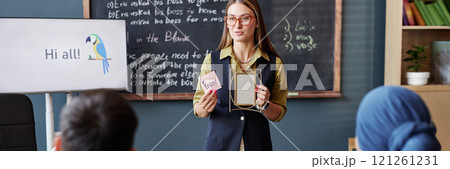 Website header shot female English teacher instructor talking to class showing adult students sticky note with word written and photo frame, while introducing new vocabulary in classroom Website header shot female English teacher instructor talking to class showing adult students sticky note with word written and photo frame, while introducing new vocabulary in classroom 121261231