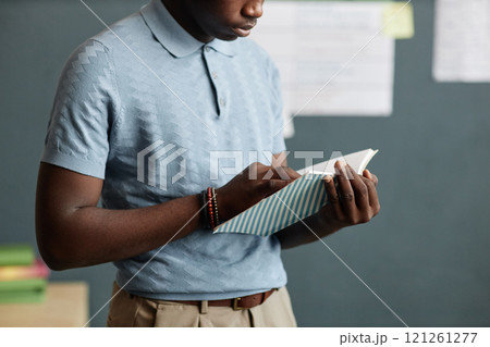 Cropped shot of young Black man with exercise book in hands reading notes while reviewing educational material before lesson in classroom, copy space Cropped shot of young Black man with exercise book in hands reading notes while reviewing educational material before lesson in classroom, copy space 121261277