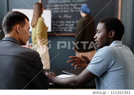 Side view of young African American boy working in pair with fellow student practicing new vocabulary in collaborative task, while improving speaking skills in class at English language school Side view of young African American boy working in pair with fellow student practicing new vocabulary in collaborative task, while improving speaking skills in class at English language school 121261361