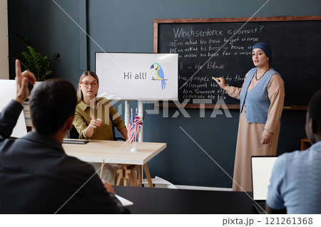 Adult Muslim woman standing at blackboard completing multiple choice task while classmate helping with hint explaining English grammar during lesson at language school Adult Muslim woman standing at blackboard completing multiple choice task while classmate helping with hint explaining English grammar during lesson at language school 121261368