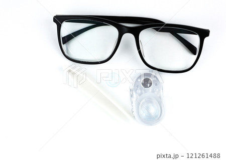 In the center of the photo, there are close-ups of black-framed glasses, behind them disposable containers with contact lenses, a blue lens and beige tweezers in close-up on a white background with In the center of the photo, there are close-ups of black-framed glasses, behind them disposable containers with contact lenses, a blue lens and beige tweezers in close-up on a white background with 121261488