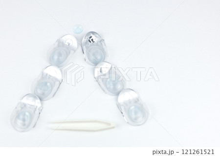 A Christmas tree made of containers with contact lenses lies on a white background, a lying lens is visible on top, and lens tweezers with space for text are at the bottom. High quality photo 121261521