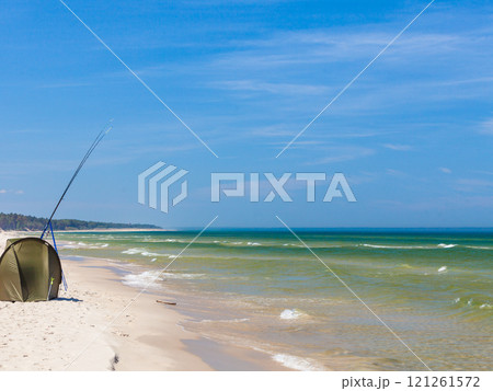 Fishing rod and tent on sea shore 121261572